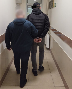 Policjant prowadzi zatrzymanego mężczyznę.