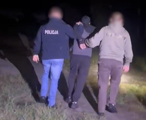 Policjanci prowadzą mężczyznę, który ma założone kajdanki na ręce z tyłu.