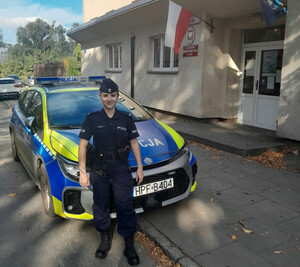 Umundurowana policjantka stoi przed radiowozem.