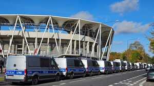 Radiowozy policyjne na tle stadionu.