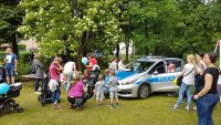 Na zdjęciu jest widoczny radiowóz policyjny, dzieci zaglądają do środka, stoją również obok radiowozu razem z rodzicami.