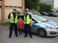 Na tle radiowozu stoją policjanci z dziewczynką.