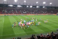 Na stadionie osoby z flagami uczestników mistrzostw biegaja po murawie.