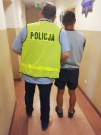 Na zdjęciu widzimy chłopaka zatrzymanego za kradzież kół , ubrany jest w jasną koszulkę i ciemne krótkie spodenki. Trzyma go policjant ubrany w żółtą kamizelkę policyjną. Zdjęcie jest zrobione na korytarzu Komisariatu II.