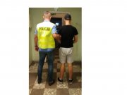 Policjant w kamizelce z napisem Policja stoi z zatrzymanym sprawca kradzieży ubranym w krótkie spodnie i czarny podkoszulek i czarna czapkę.