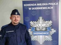 umundurowany w granatowym uniform policjant stoi przy roll-up z napisem Komenda Miejska Policji w Skierniewicach