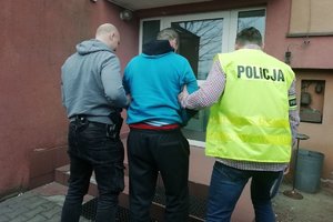 Mężczyzna, policjant w kamizelce z napisem policja i policjant z bronią bez munduru wchodzą do budynku