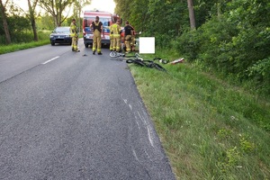 miejsce wypadku drogowego, pogięte rowery leżą na asfalcie, obok karetki stoją strażacy i ratownicy medyczni