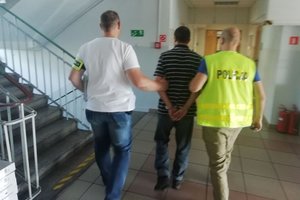 Dwóch policjantów prowadzi mężczyznę z kajdankami na rękach z tyłu