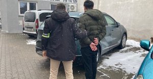Policjant i mężczyzna z kajdankami na tle samochodów.