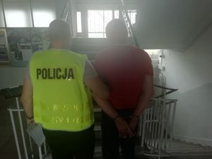 Mężczyzna z kajdankami na rękach z tyłu i policjant.