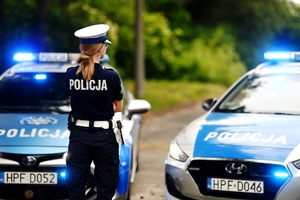 Policjantka na tle radiowozów.