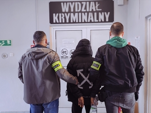 Zatrzymany z policjantami, w tle napis wydział kryminalny.