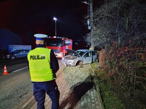 Policjant podejmujący czynności na miejscu zdarzenia, w tle rozbite auto.