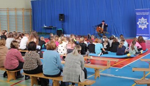 Na hali sportowej grupa dzieci i mężczyzna z gitarą.