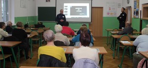 W sali szkolnej policjanci przeprowadzają pogadankę z seniorami.