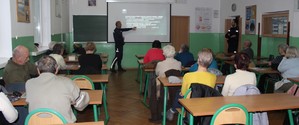 W sali szkolnej policjanci przeprowadzają pogadankę z seniorami.
