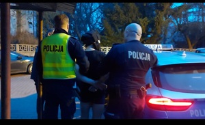 Dwóch umundurowanych policjantów trzyma osobę zatrzymaną.