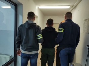 Dwóch policjantów trzyma zatrzymanego.