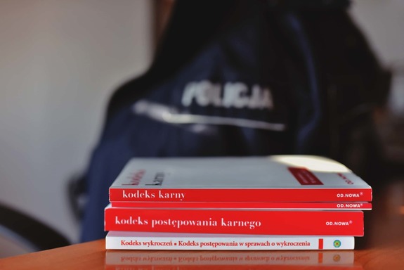 Na zdjęciu widać bok umundurowanego policjanta i przed niem kodeksy.