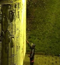 mężczyzna w kapturze maluje coś na ścianie pomnika