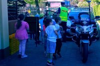 zdjęcie przedstawia dzieci oglądające policyjny radiowóz i motocykl. Na zdjęciu widać również umundurowanego policjanta