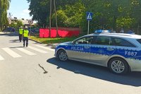 Stojący radiowóz oraz policjanci wykonujący czynności w miejscu wypadku drogowego.