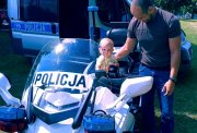 Roczne dziecko siedzi na policyjnym motocyklu, obok stoi jego ojciec.