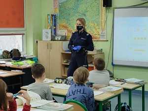 Policjantka stoi w klasie, naprzeciwko niej znajduje się grupa dzieci.