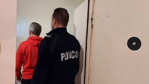 Policjant stoi z zatrzymanym mężczyzną ubranym w czerwoną bluzę.