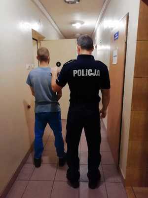 Umundurowany policjant stojący z zatrzymanym mężczyzną.