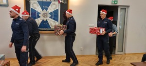Policjanci niosący pod choinkę prezenty.