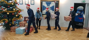 Policjanci, policyjna maskotka garnizonu łódzkiego i Starosta Powiatu Pabianickiego niosący pod choinkę prezenty.