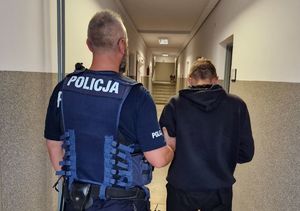 Policjant stojący na korytarzu komendy z zatrzymanym mężczyzną.