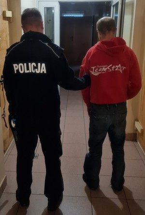 stojący tyłem policjant z zatrzymanym mężczyzną.