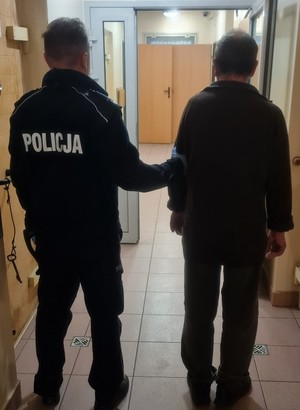 stojący tyłem policjant z zatrzymanym mężczyzną.