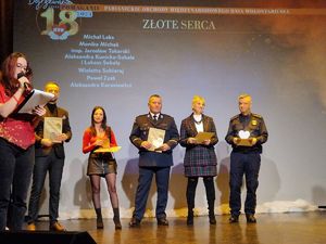Komendant Powiatowy Policji w Pabianicach stoi na scenie pośród innych laureatów nagrody Złotego Serca.