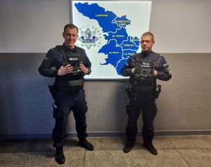 Dwaj umundurowani policjanci stojący przy podświetlonej mapie powiatu pabianickiego.