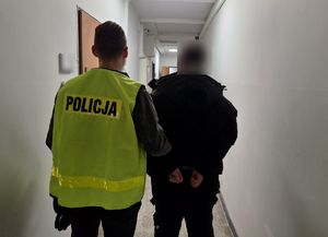 Nieumundurowany policjant w kamizelce odblaskowej z napisem Policja stoi wraz z zatrzymanym nieletnim.