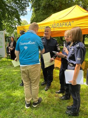 Komendant Powiatowy Policji w Pabianicach wręcza uczestnikowi pamiątkowy dyplom, obok stoją dwie policjantki.