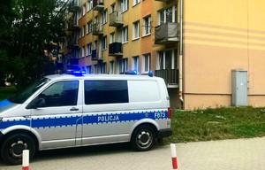Radiowóz na tle stojącego bloku.