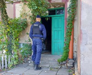 Policjant stojący przed wejściem do budynku, w którym doszło do zbrodni.