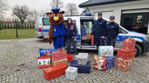 Mundurowi stoją z maskotką pabianickiej policji i z członkinią organizacji charytatywnej Połóż Serce na Dłoni na tle oznakowanego radiowozu, w którym znajdują się prezenty dla dzieci z rodzin dotkniętych powodzią.