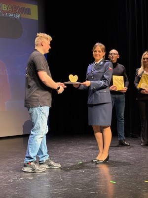 Policjantka odbiera z rąk wolontariusza statuetkę.