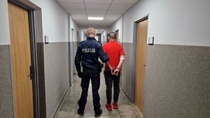 Policjant stoi na korytarzu z zatrzymanym mężczyzną.