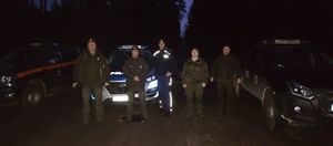 Policjant wraz z innymi służbami stoi na tle pojazdów służbowych.