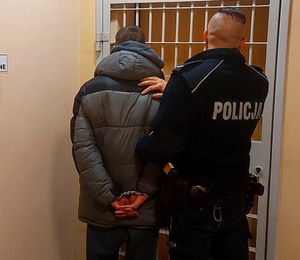 Umundurowany policjant stoi z zatrzymanym mężczyzną.