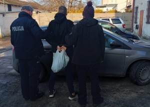 Umundurowany policjant i nieumundurowana policjantka stoją z zatrzymanym mężczyzną.