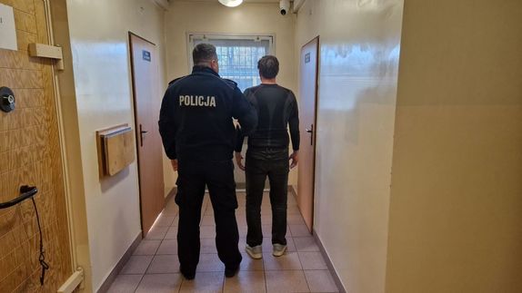 Umundurowany policjant stoi z zatrzymanym mężczyzną.