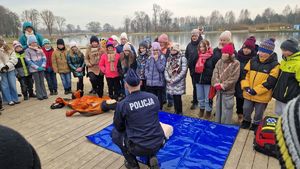 Policjant pokazuje na fantomach jak wykonać pierwszą pomoc. Dookoła stoją zgromadzone dzieci.